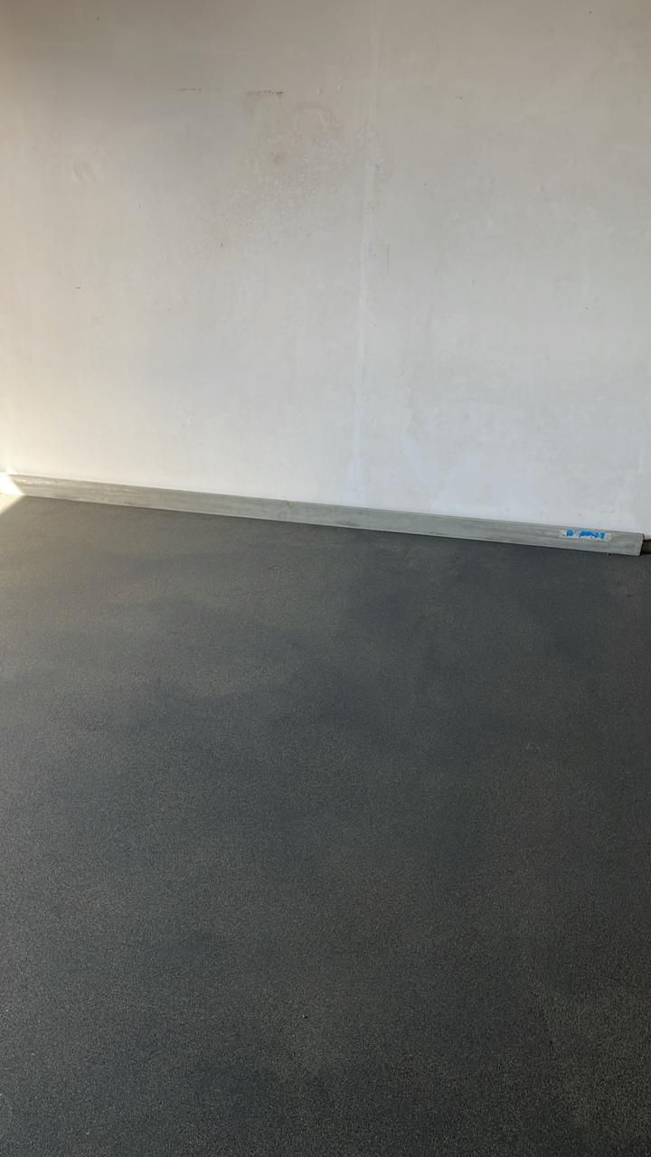 Стык тёмно-серой стяжки с белой стеной и уровнем у основания.