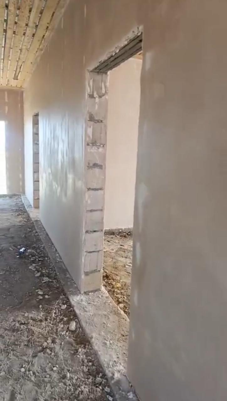 Свежештукатуренная колонна с выводом электрики и окном на заднем плане.