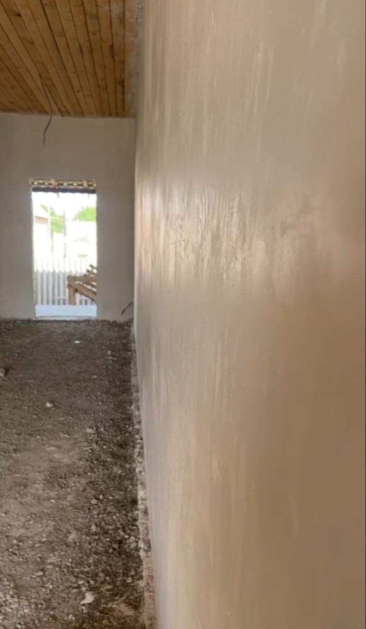 Длинная штукатуренная стена с гладкой поверхностью и дверным проёмом на заднем плане.