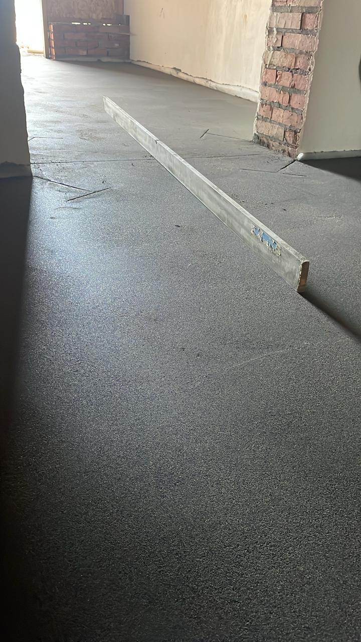 Длинный коридор со свежей стяжкой, правилом и кирпичным проёмом.